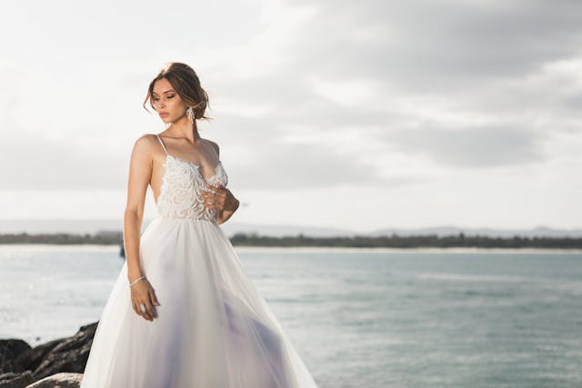 A bride in a wedding dress standing on rocks by the ocean, perfect for weddings in New Zealand