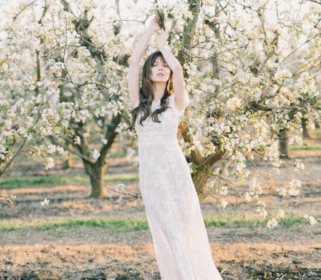 A bride in a white long sleeve wedding dress standing in an apple orchard