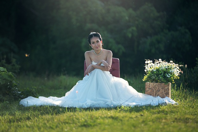 A pregnant bride in a white wedding gown sitting on green grass for maternity photoshoot in New Zealand