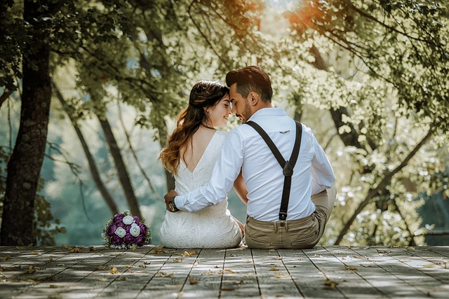 Bride and groom sitting on wooden bridge, surrounded by nature